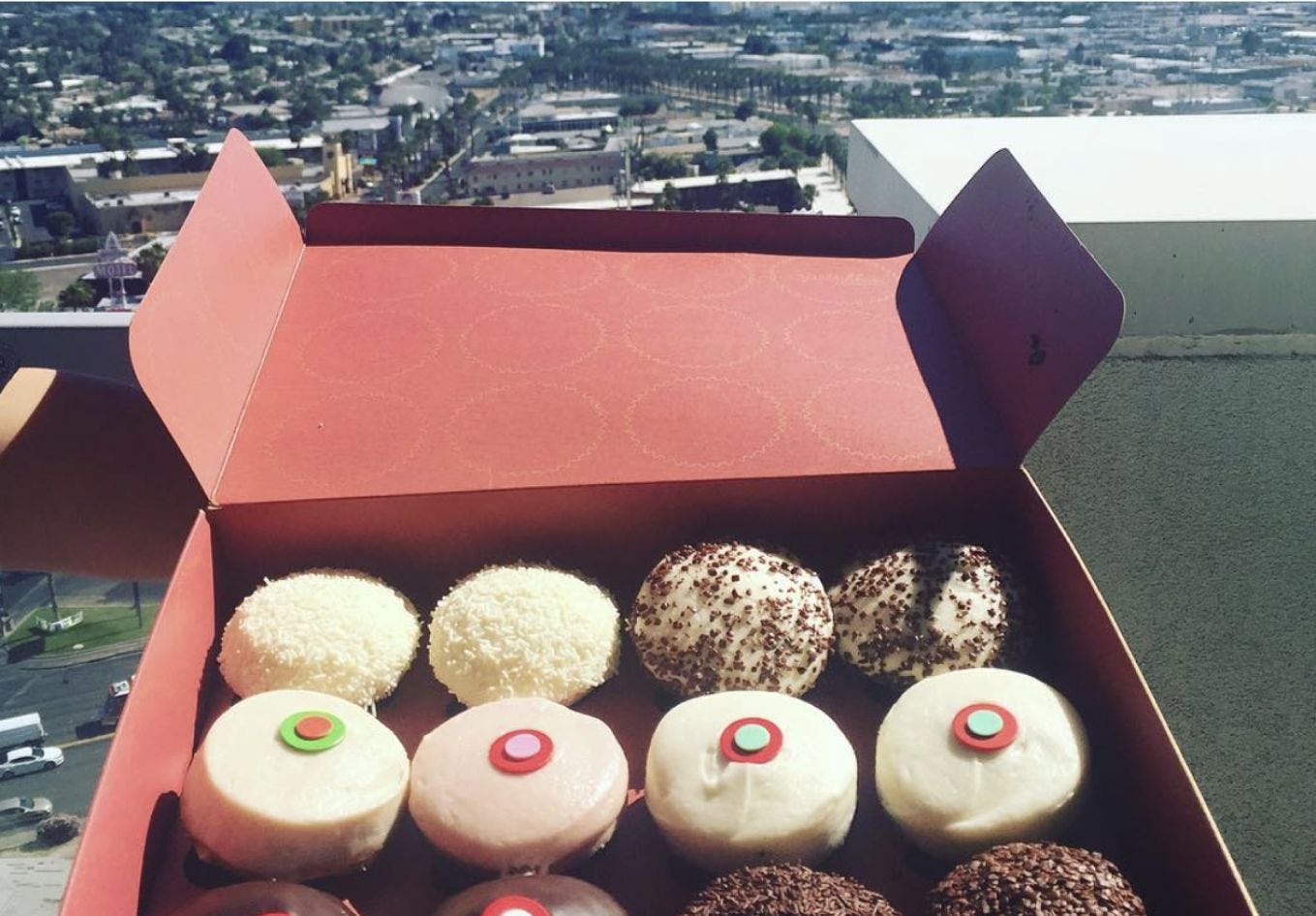 Box of delicious looking donuts overlooking a city from a rooftop. 